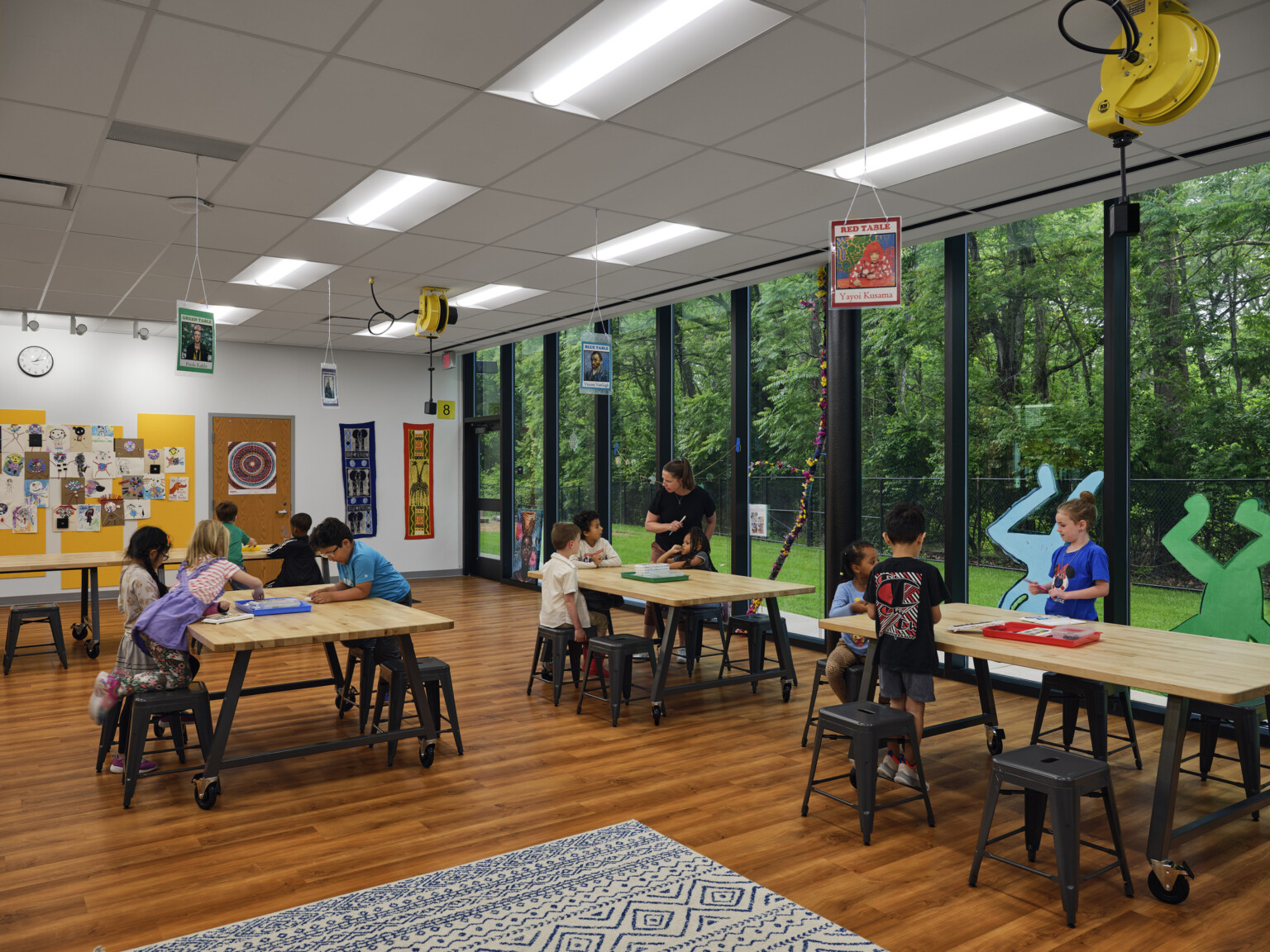 Elementary school classroom filled with tables and chairs with a large wall of windows