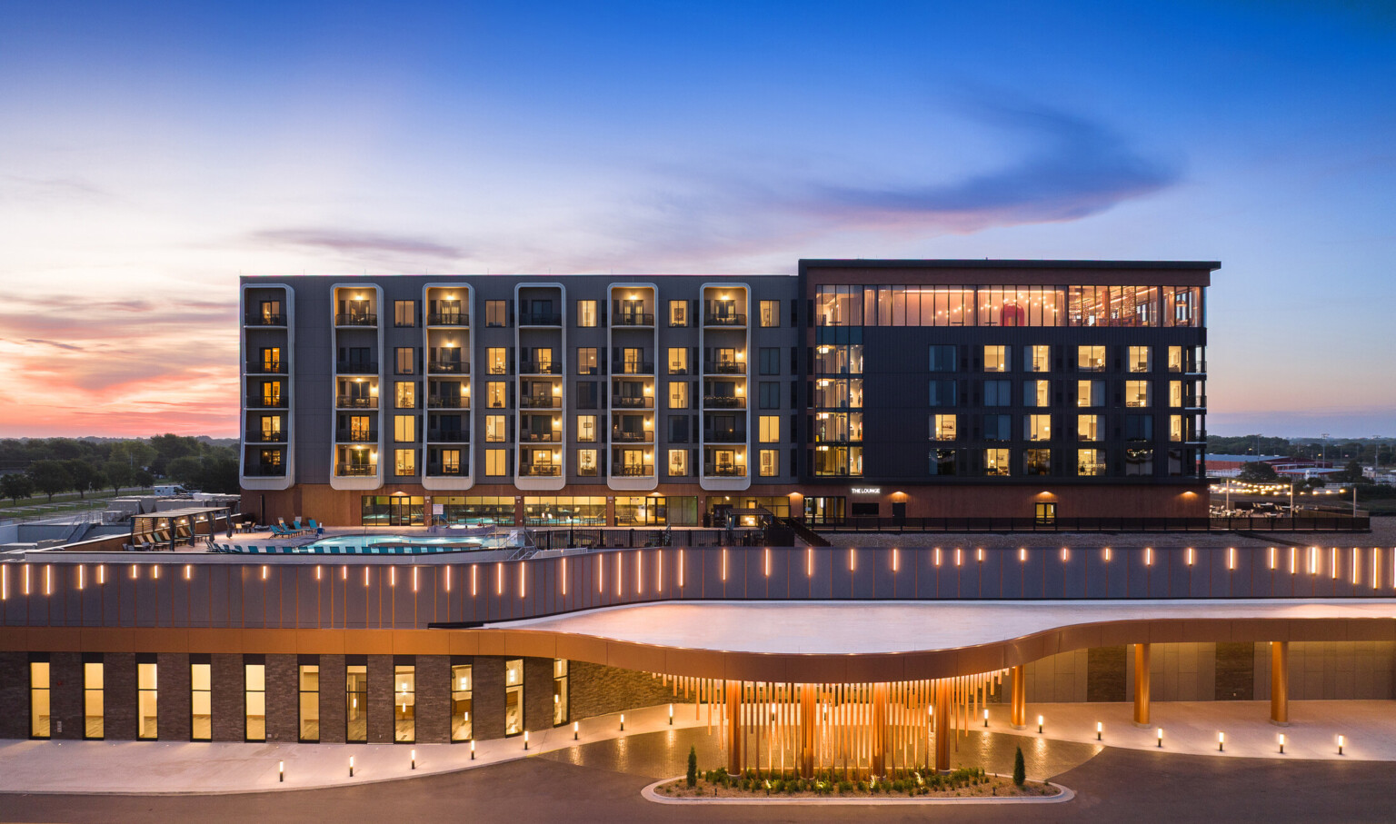 modern tower Resort building and pool deck illuminated at dusk, with entrance in view; front entrance image of Grand Island Casino Resort at Fonner Park