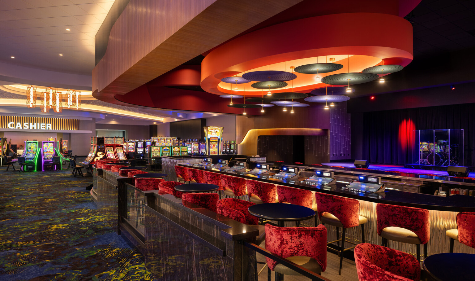 Grand Island Casino Resort at Fonner Park showroom lounge with glowing, iridescent finishes; red velvet cocktail chairs and tables under read feature lighting