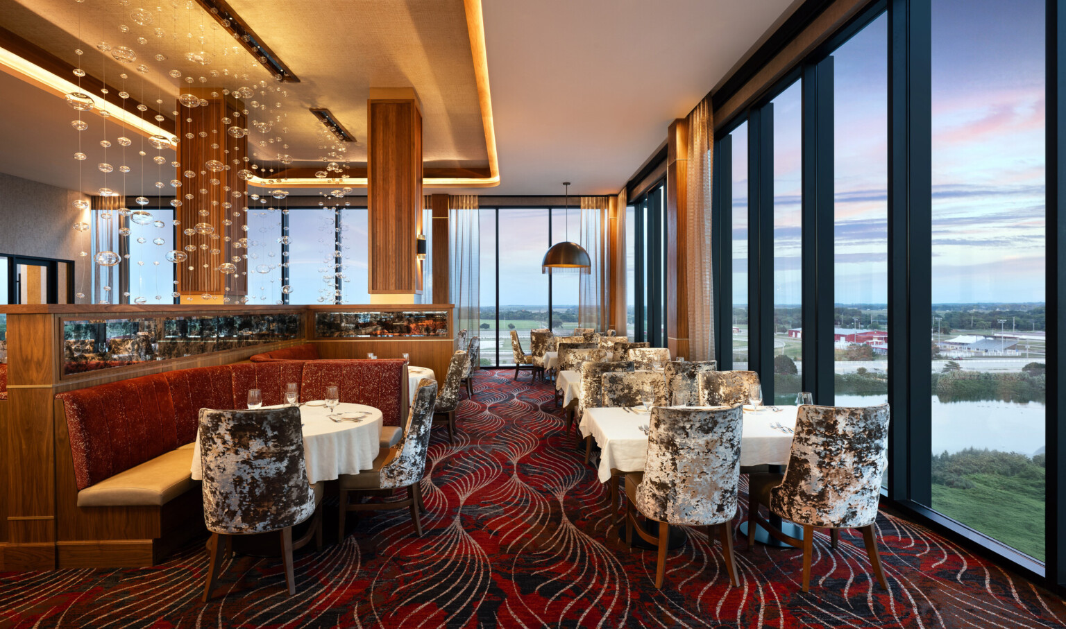 Grand Island Casino Resort at Fonner Park Steakhouse restaurant with white cloth table over looking floor to ceiling windows at dusk; warm red and wood tones, gold-domed chandeliers, booths, views toward the racetrack.