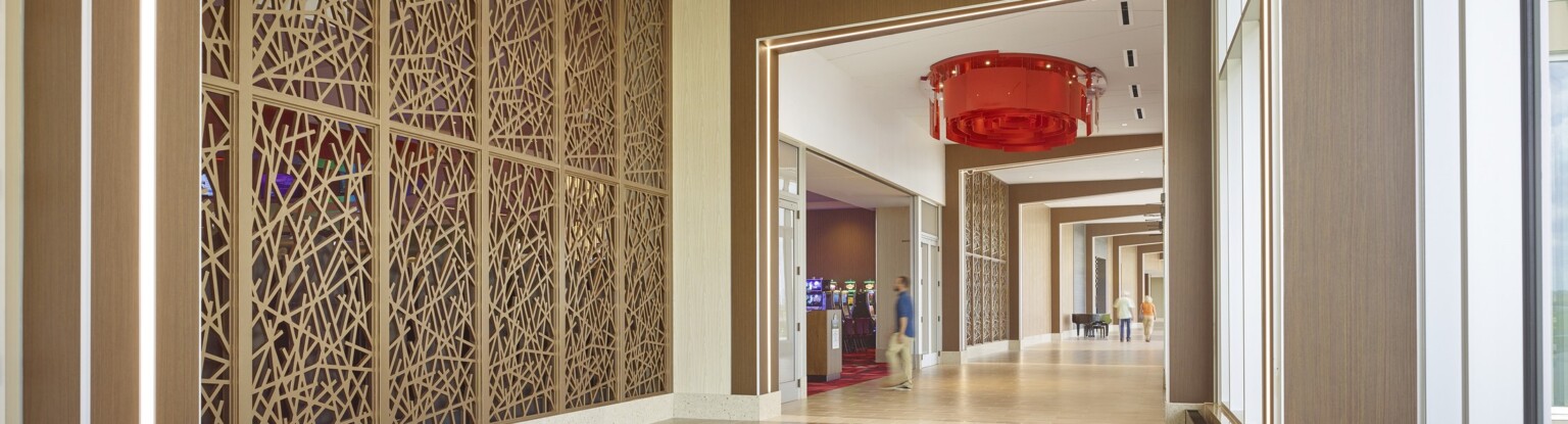 Modern interior corridor with geometric wooden lattice walls, tiled floor, and large windows. A red chandelier hangs from the ceiling