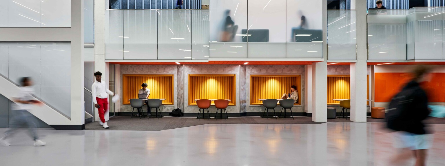 interior school atrium; double height floor with collaboration tables on the first floor, private meeting rooms on the second floor; soft lighting and branding colors adorn the space