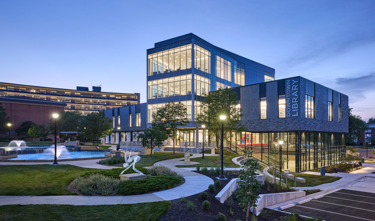 exterior shot of Olathe Downtown Library; multi-level exterior building facade with large floor to ceiling windows; front green area with sculptures and seating
