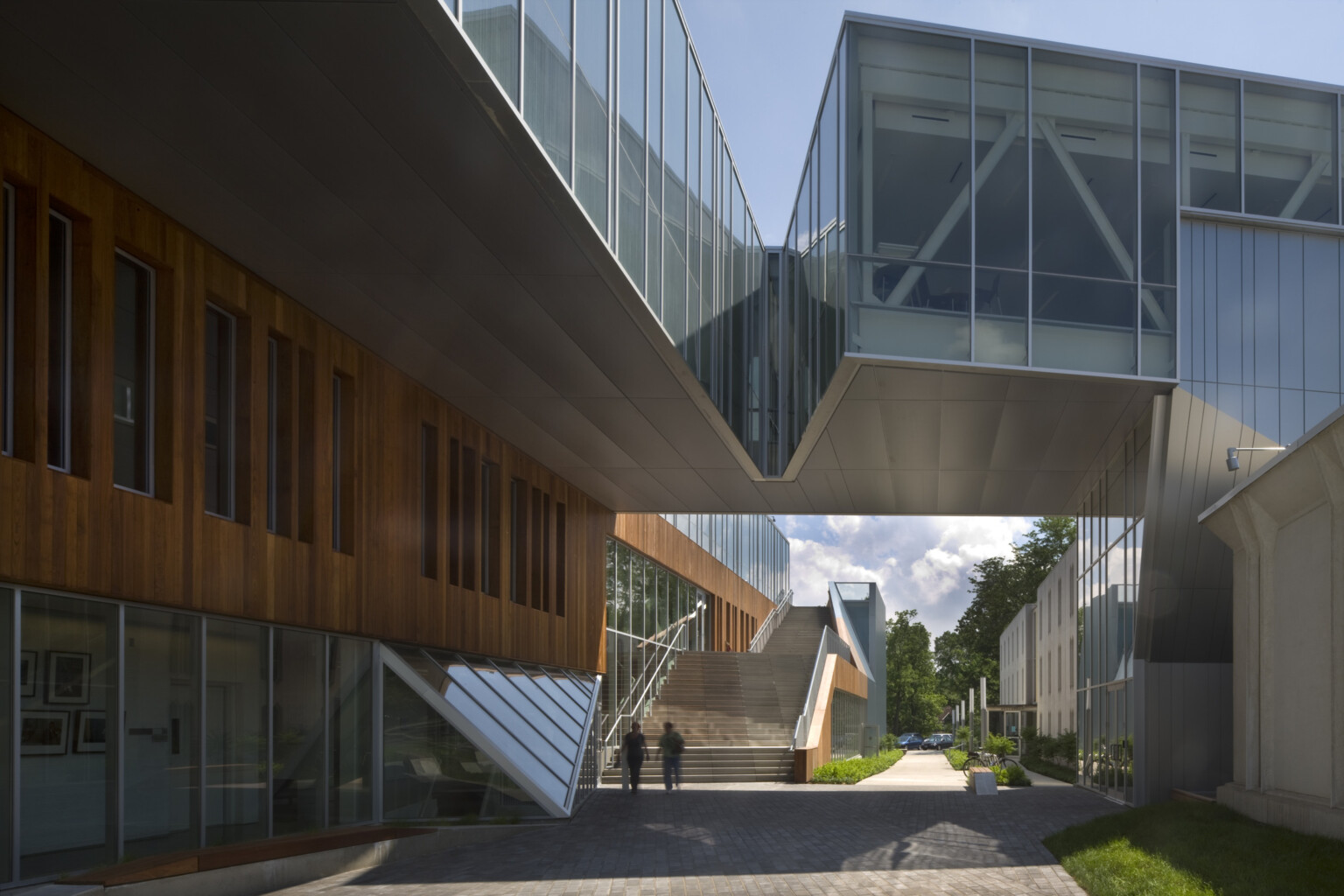 Partially covered walkway between buildings, building at left has first floor window walls below wood panels; dlr group design
