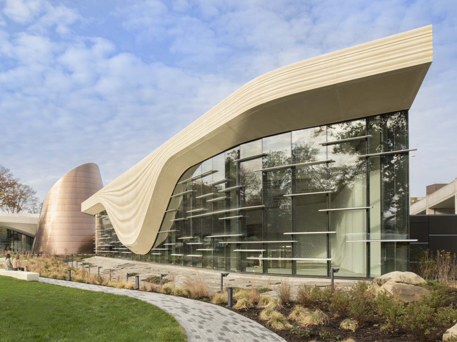Front facade of the Cleveland Museum of Natrual History; a geometric cream colored concrete structure outlines the large windows of the building to look like a glacier; backdropped by clear blue skies
