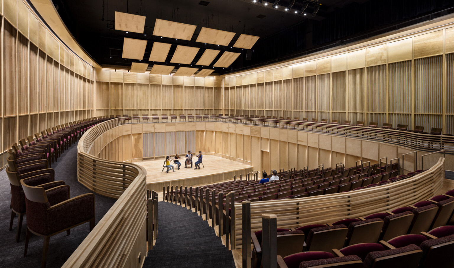 View from the back of wooden wall oval auditorium with 4 musicians on stage and 2 people seated in the audience