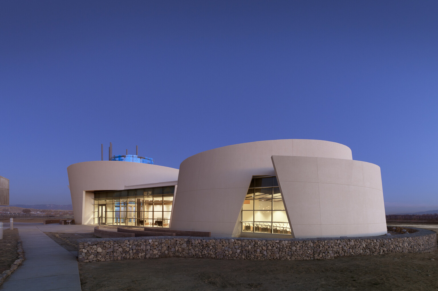 community and culture at dine college library, desert structure with an iconic design. Curved structure overlays itself and lit up from within with warm lights; dlr group design
