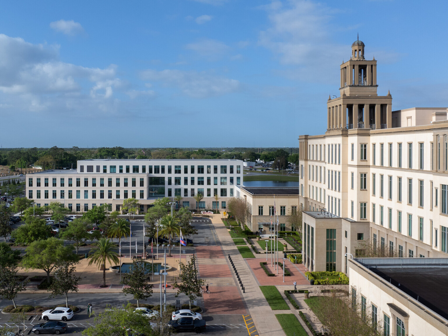 Large four-story courts building with three tiered cupola occupies the right side of the image. In the center and foreground, a parking lot and public plaza with fountain stand before a 4-story government building in front of a lake.