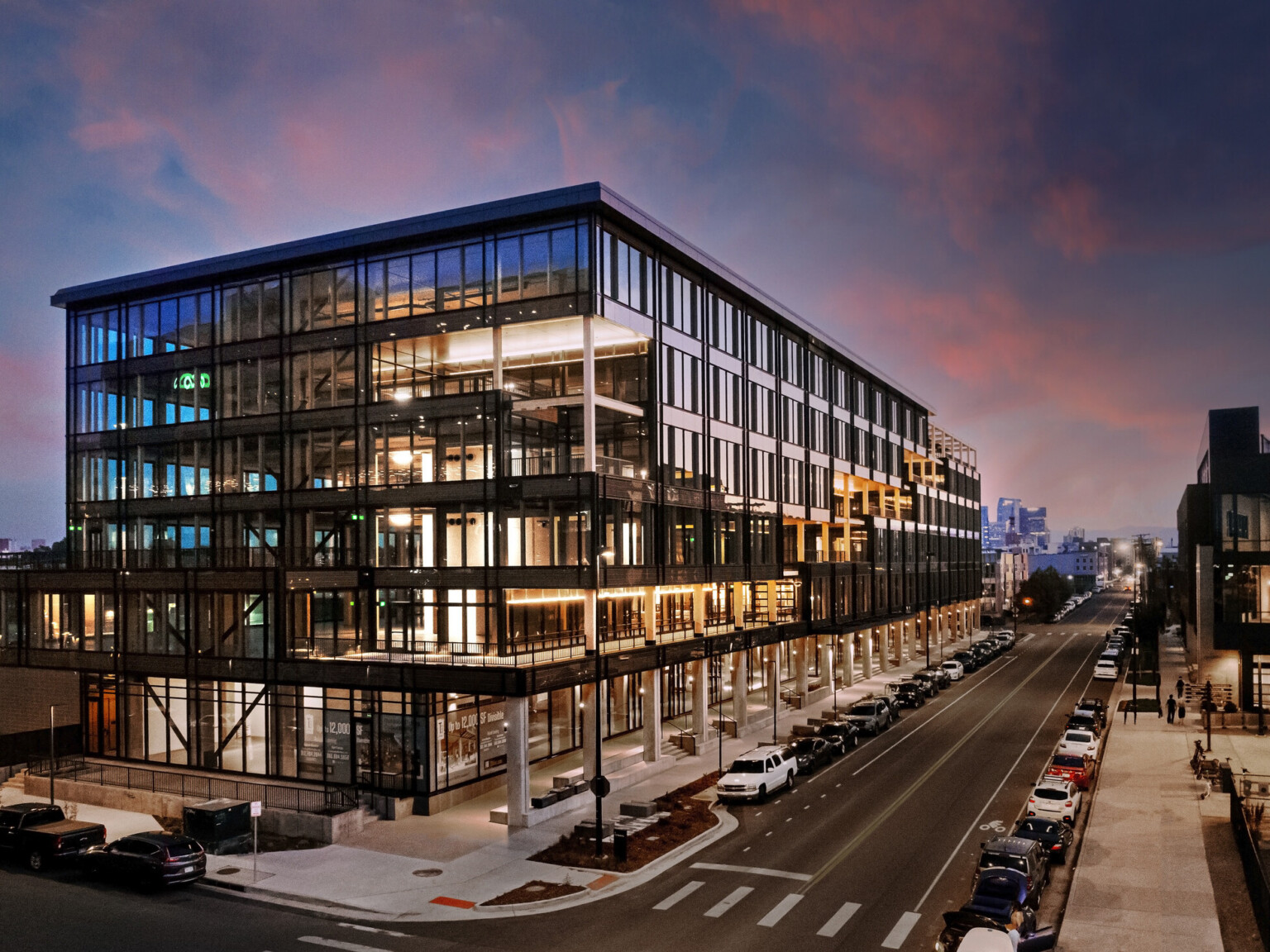 Industrial Mass Timber building at sunset; full floor to ceiling glass windows on every floor surrounded by structural elements; pedestrian walking space below