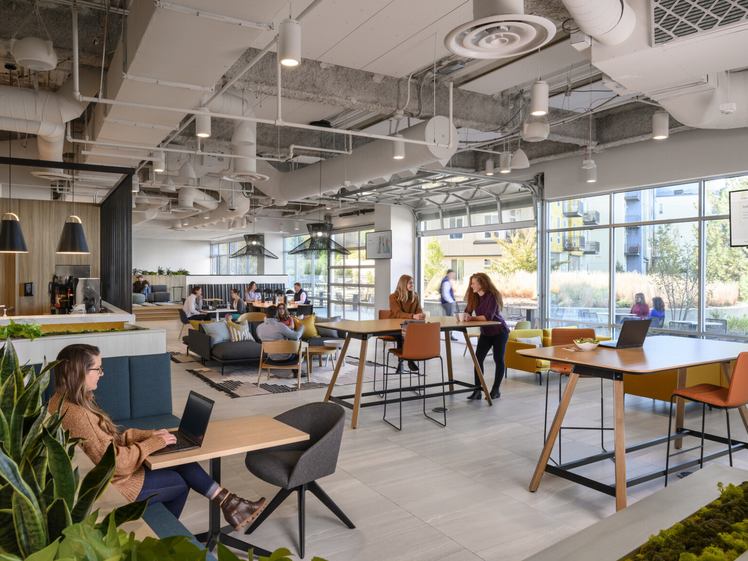 Mixed seating with tables in room with floor to ceiling windows with open garage style door, right. Coffee counter to left
