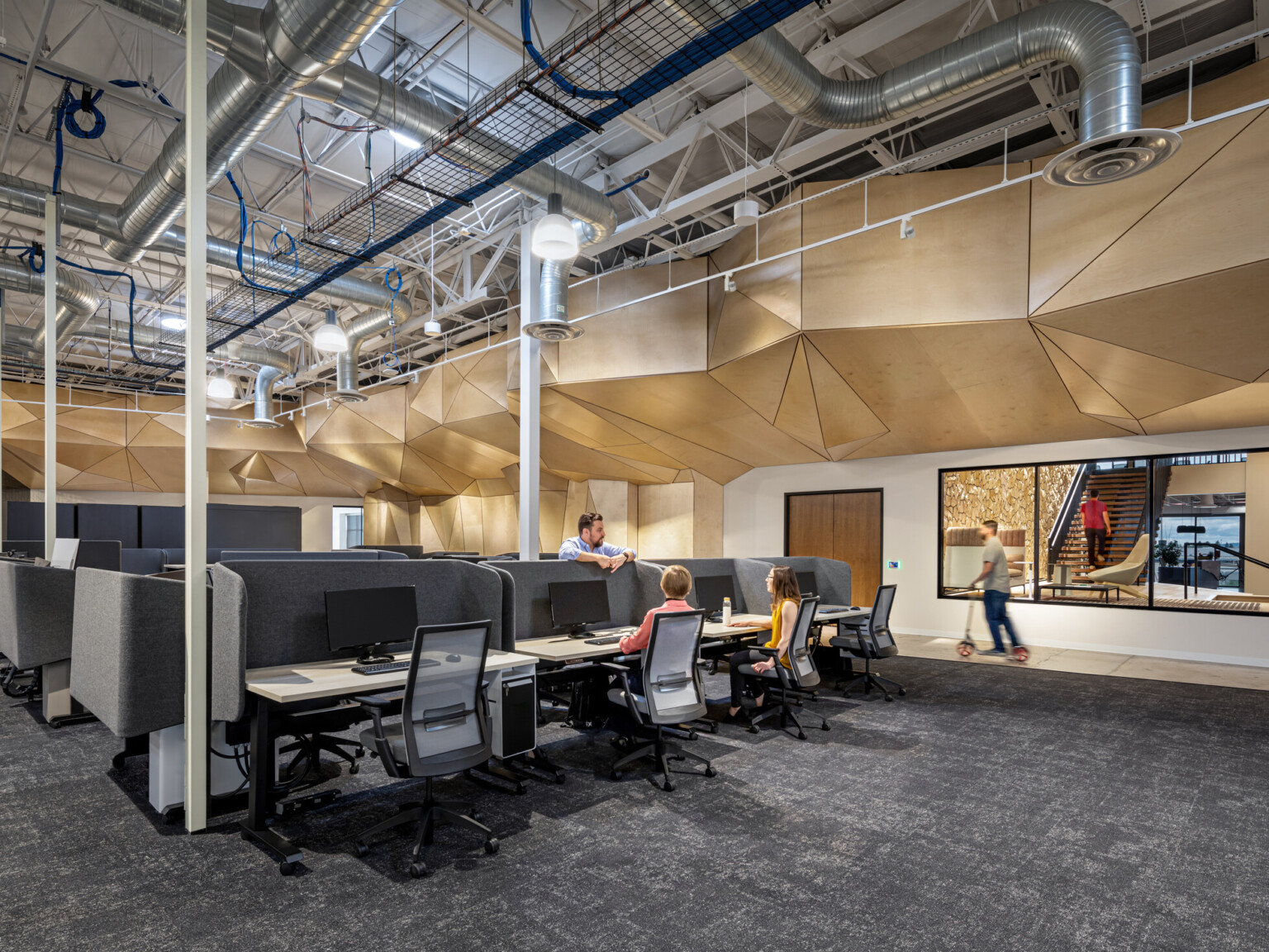 interior of a workplace with open desking, sculptural wood ceiling, and exposed ductwork