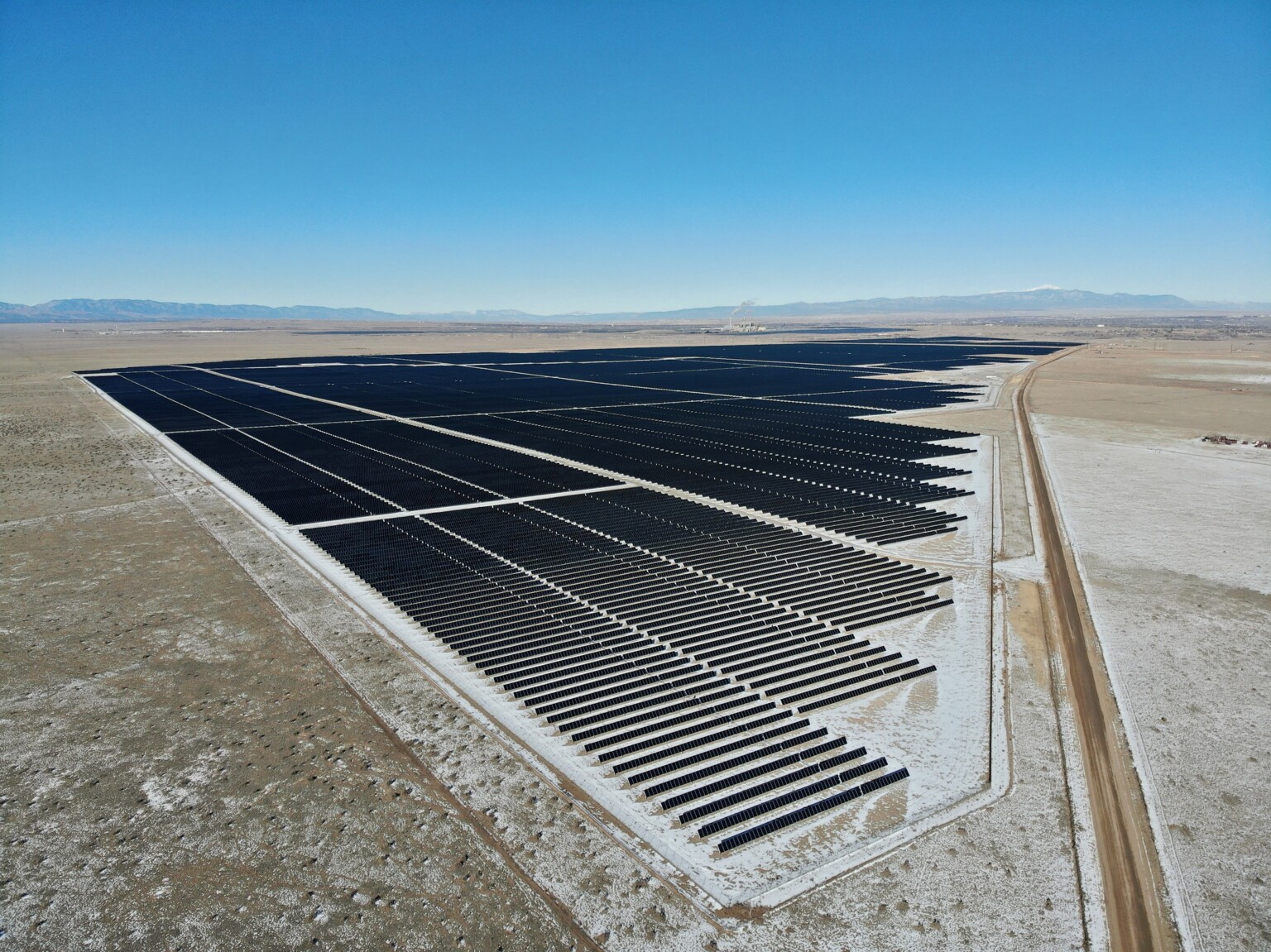 aerial view of a solar panel field; dry arid vacant flatlands surround with mountains in the background