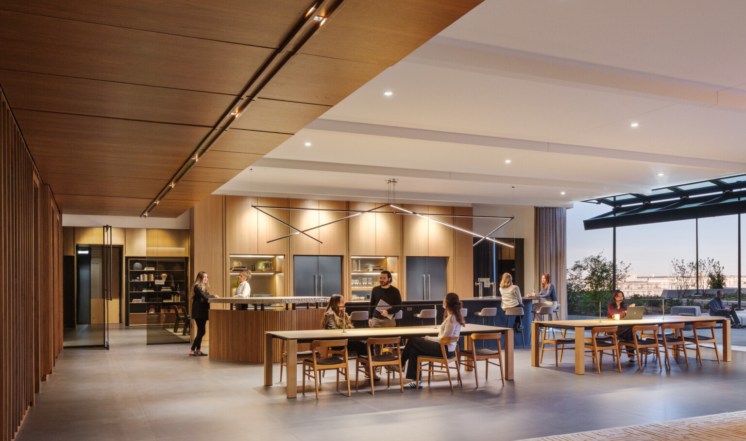 A modern office space with wooden decor, people interacting at tables, and large windows offering outdoor views.