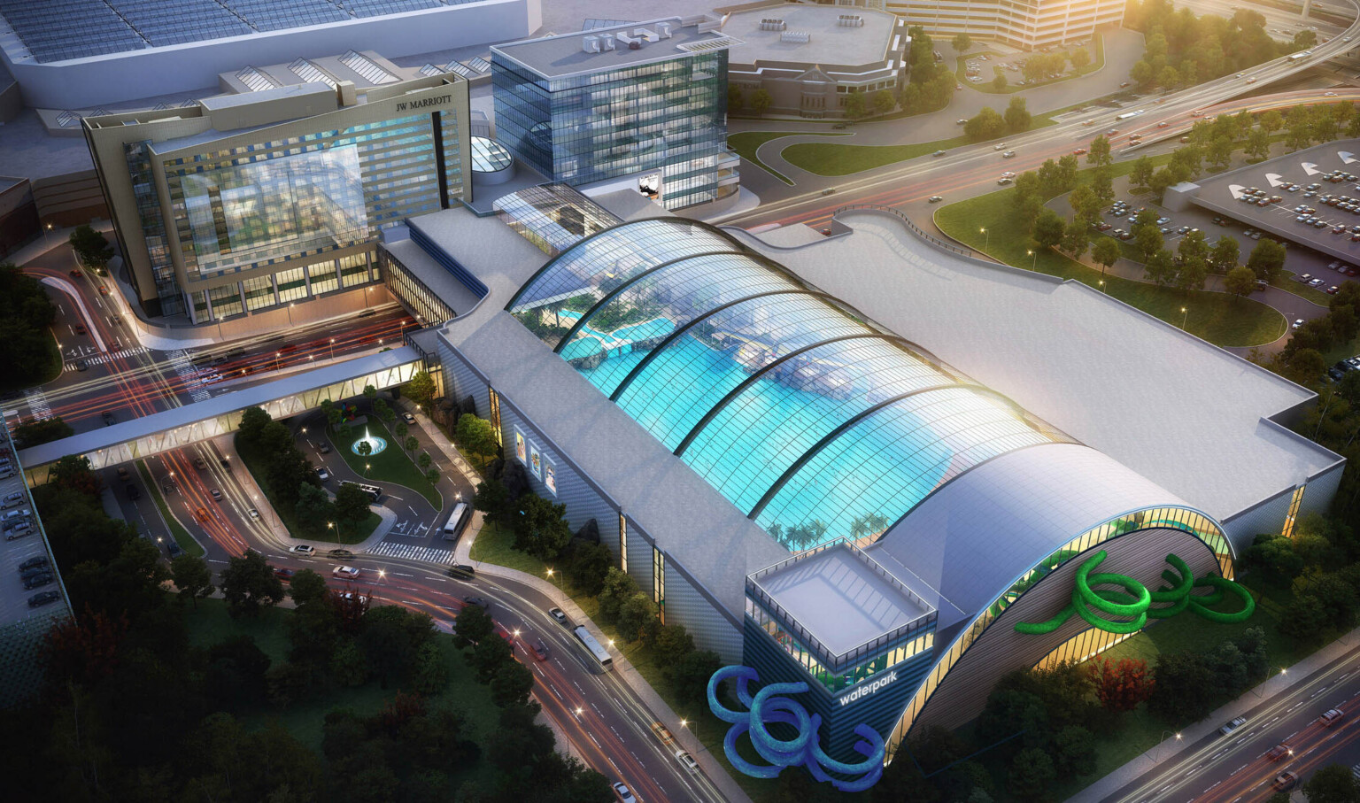 Aerial view of indoor waterpark with arching skylights over roof. Blue and green water slides curl out sides of grey building