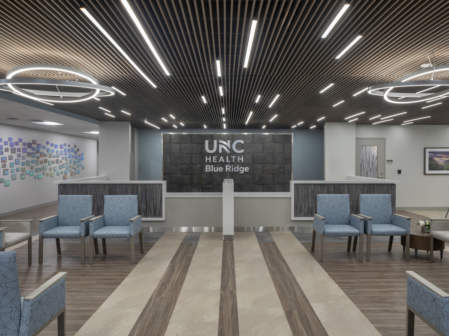 Medical waiting room filled with blue chairs, modern circular lighting hanging from the ceiling, and UNC Health Blue Ridge on the back wall
