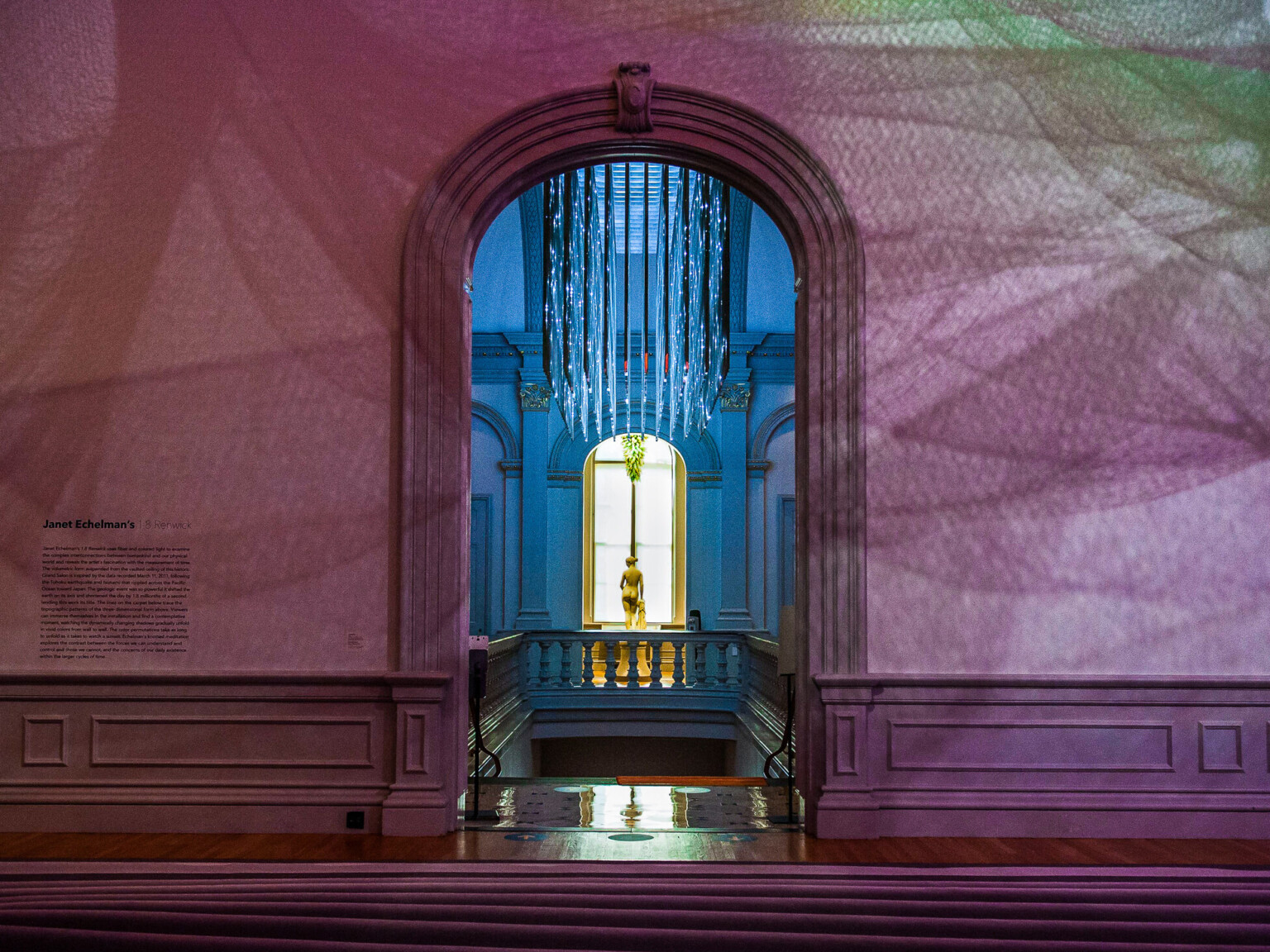 Arched doorway framing a statue lit by natural light, with patterned shadows on classical walls.