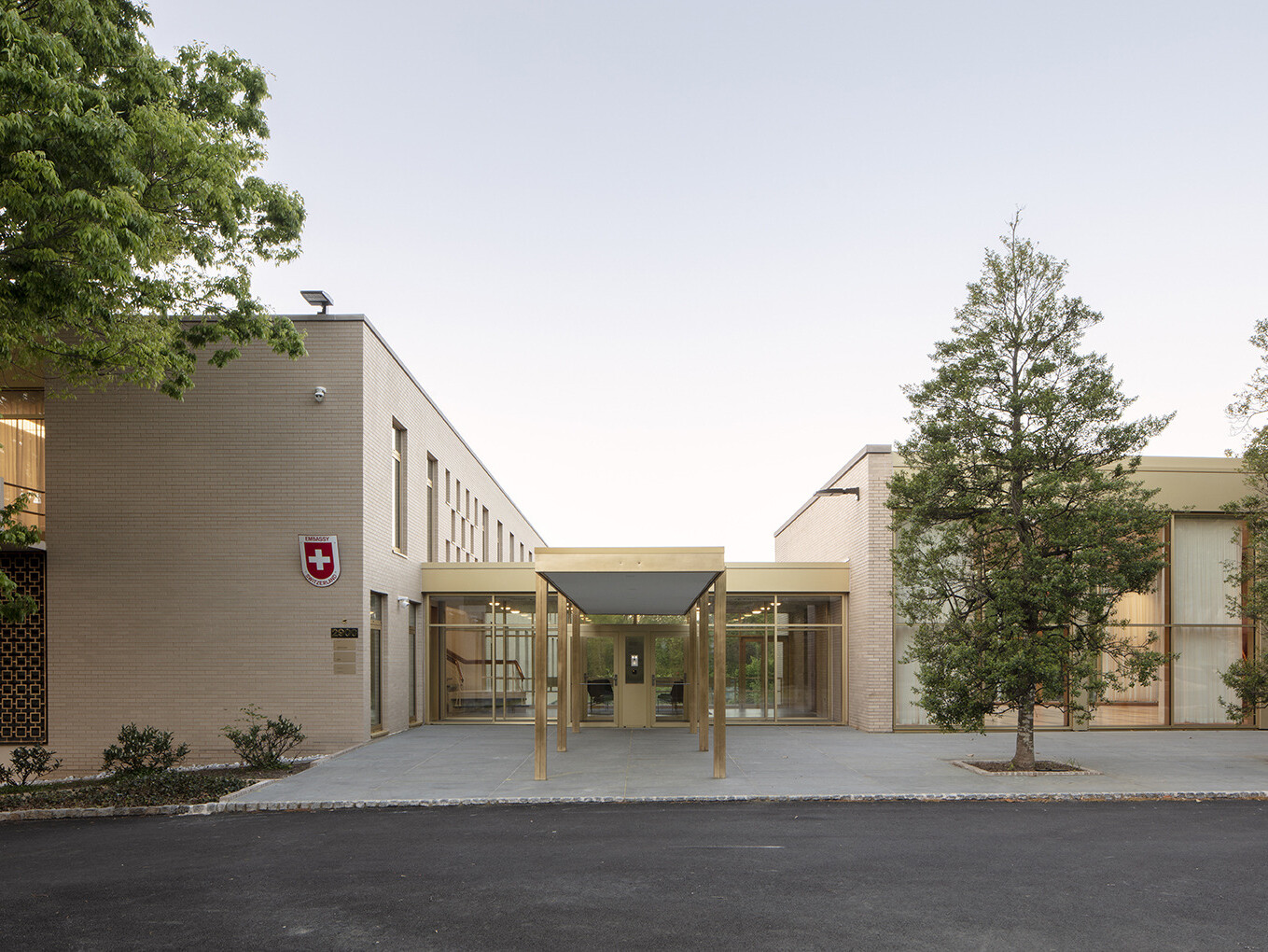 Exterior of a light brick multistory building with brushed gold accents, awning that extends from glass entryway