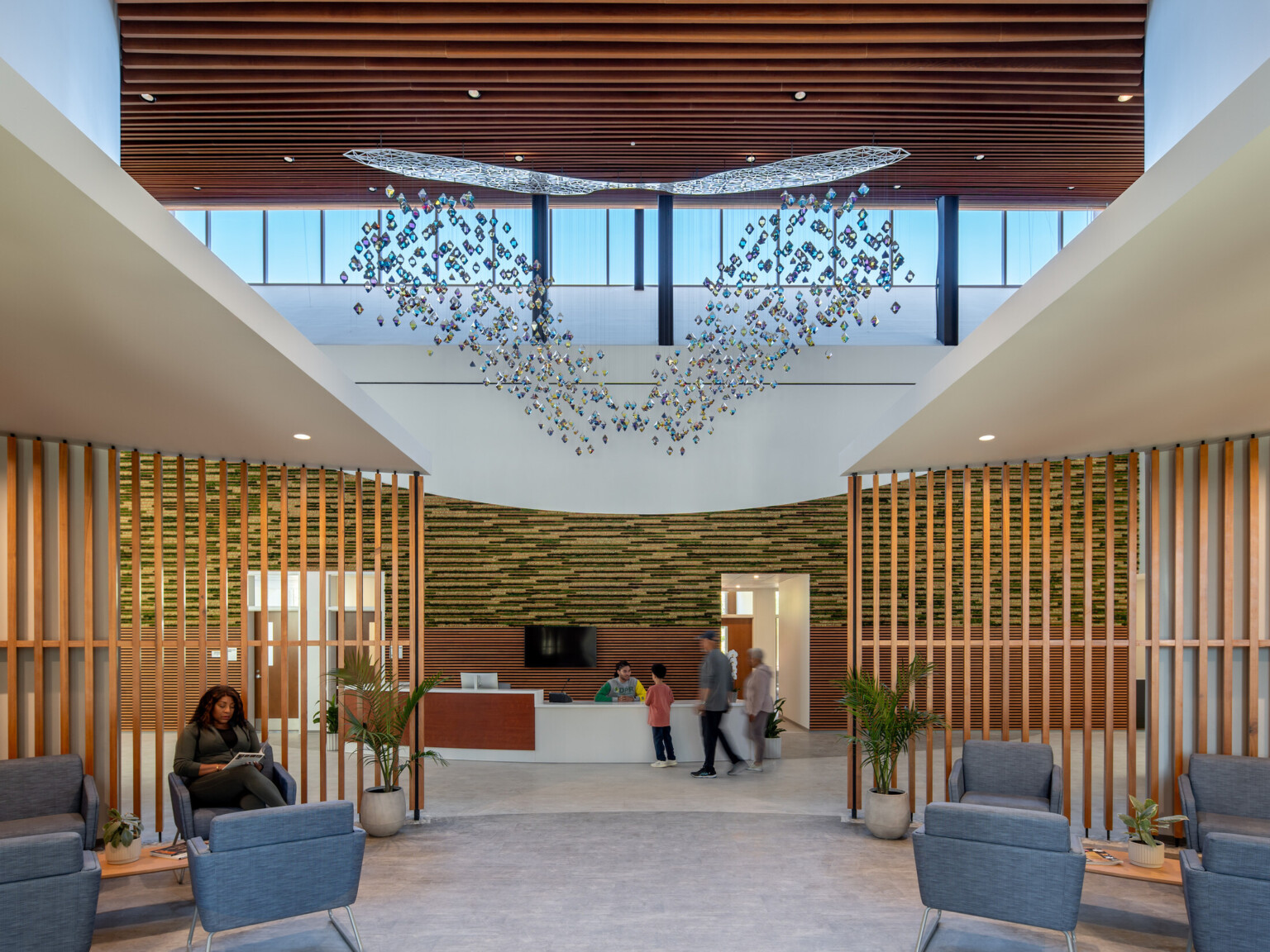 Medical office waiting room with modern fixture suspended from ceiling, wooden accent wall dividing seating area and desk area