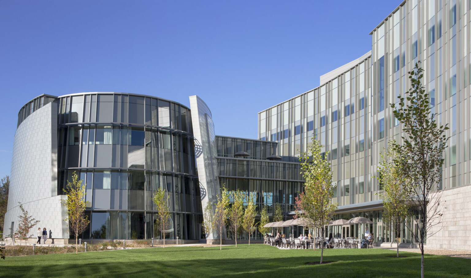 exterior of a world renowend genomic medical center in Connecticut; round glass from anchors one end of the building with an outdoor patio beneath facade with glass fenestration