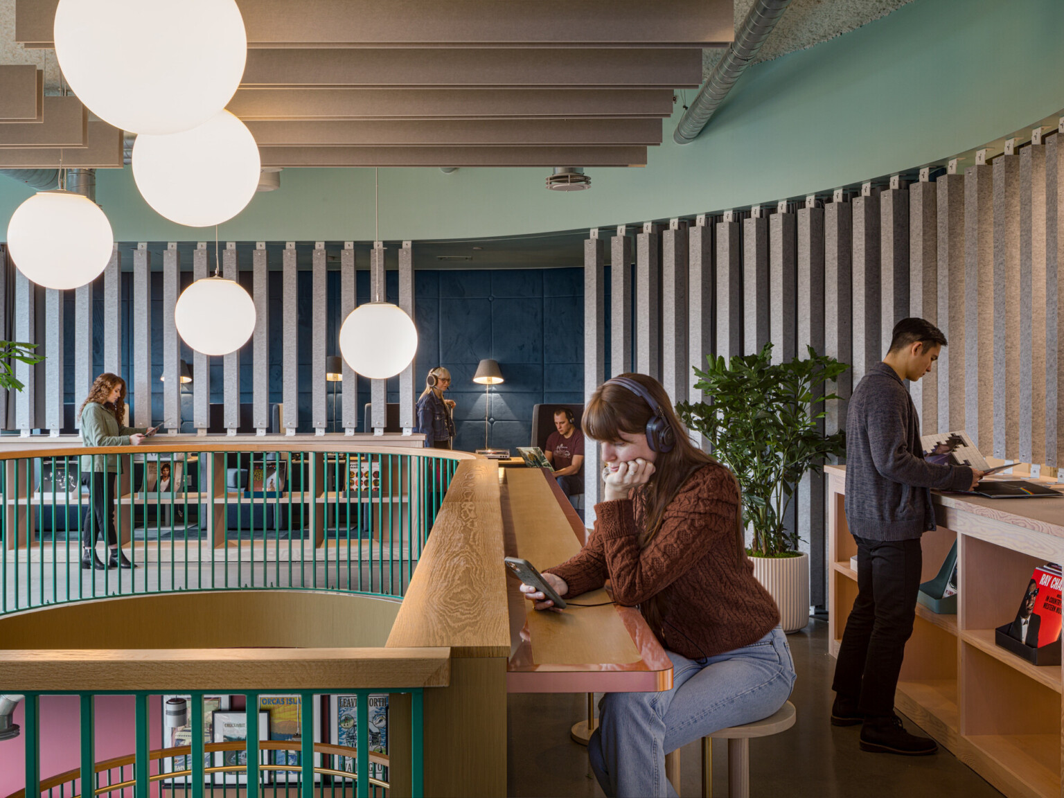 a woman on her phone with headphones sits at a radial wooden counter overlooking a mezzanine finished in wooden slats