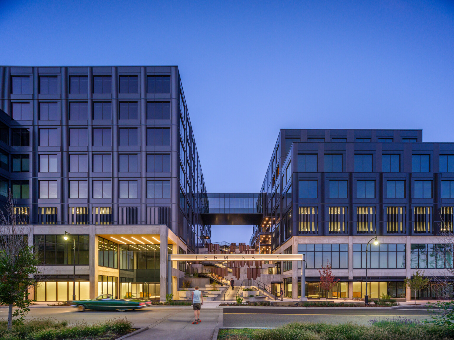 night view of multiple story mixed-use development, two large buildings connected by skyway, elevated bridgeway