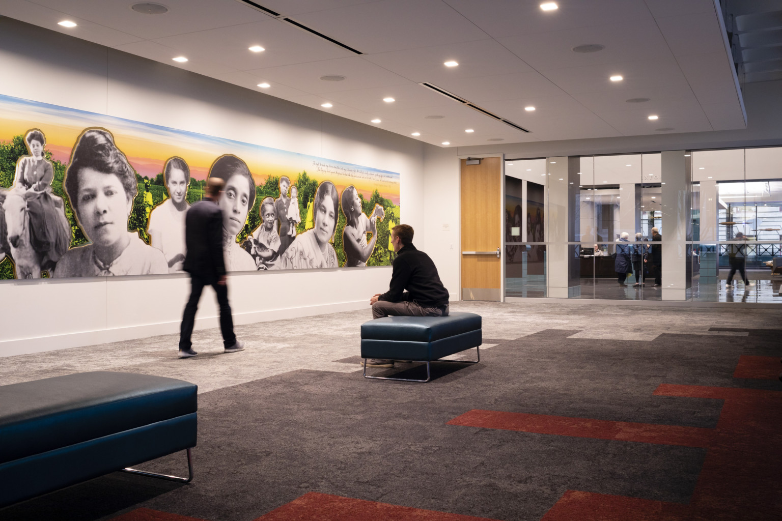 First floor event space with geometric carpet, a man sits looking at a large colorful mural, portland building renovation, restoration, postmodern architecture, michael graves architecture
