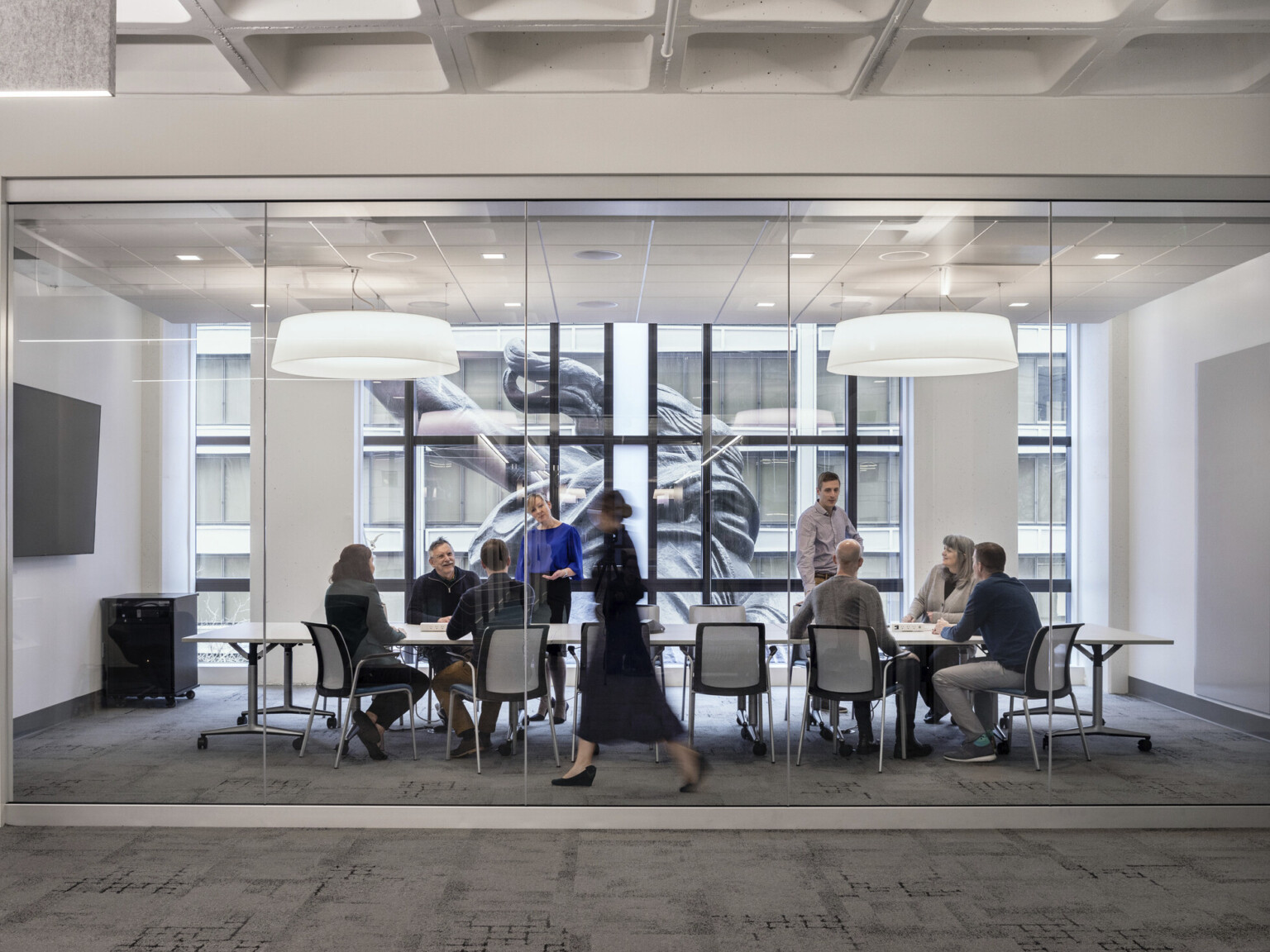 A conference room with glass wall into hallway has floor to ceiling windows looking onto the back of the Portlandia sculpture