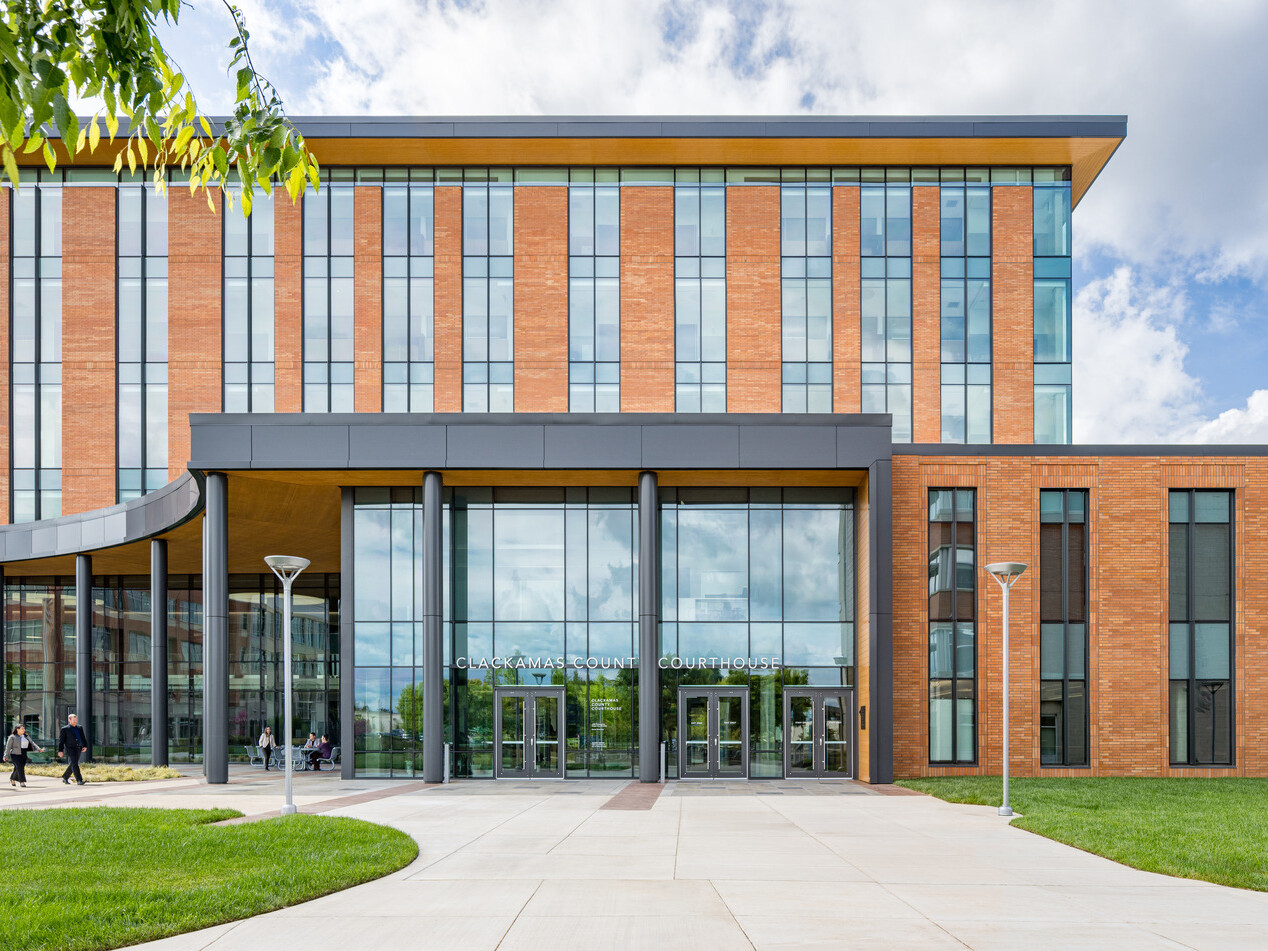 Front of a modern courthouse building featuring a mix of tan brick and expansive glass panels. Glass entrance is framed by a dark, horizontal overhang and vertical columns