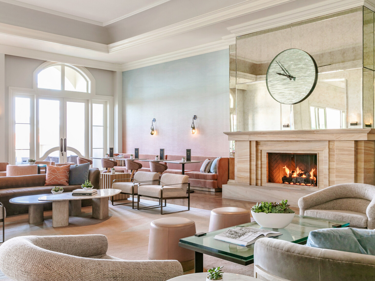 modern and airy beach resort lobby with muted tones, fireplace, large clock on a mirrored wall, and scones lighting the space