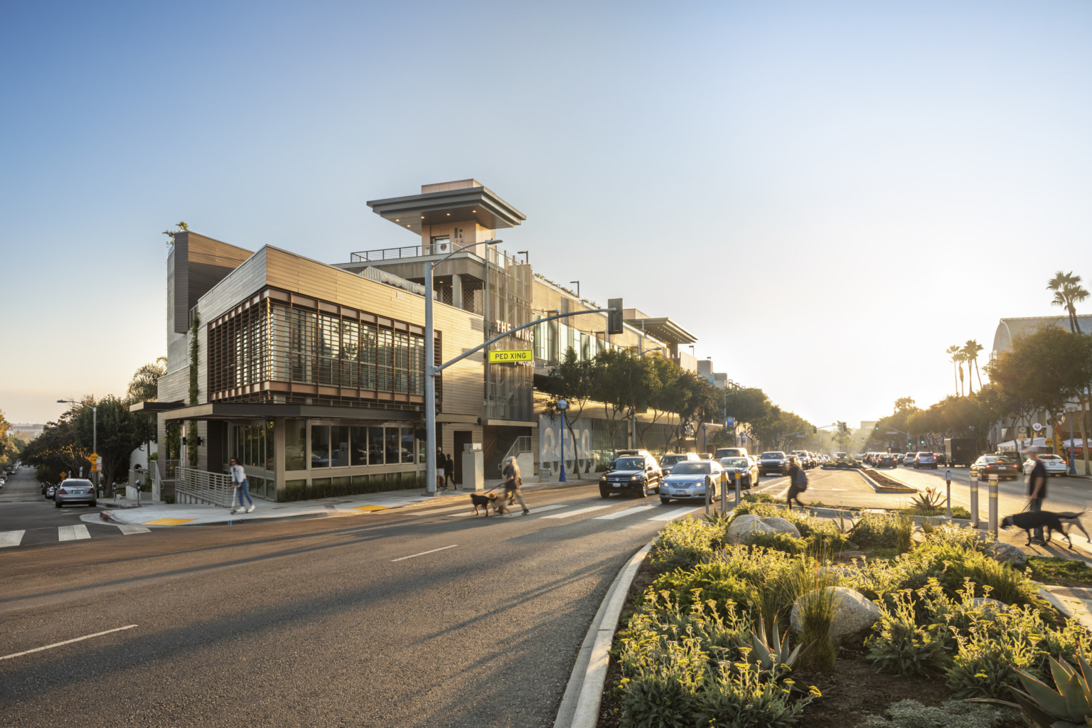 Pedestrians cross street toward 8550 Santa Monica Blvd, a concrete three-story building with retail and dining