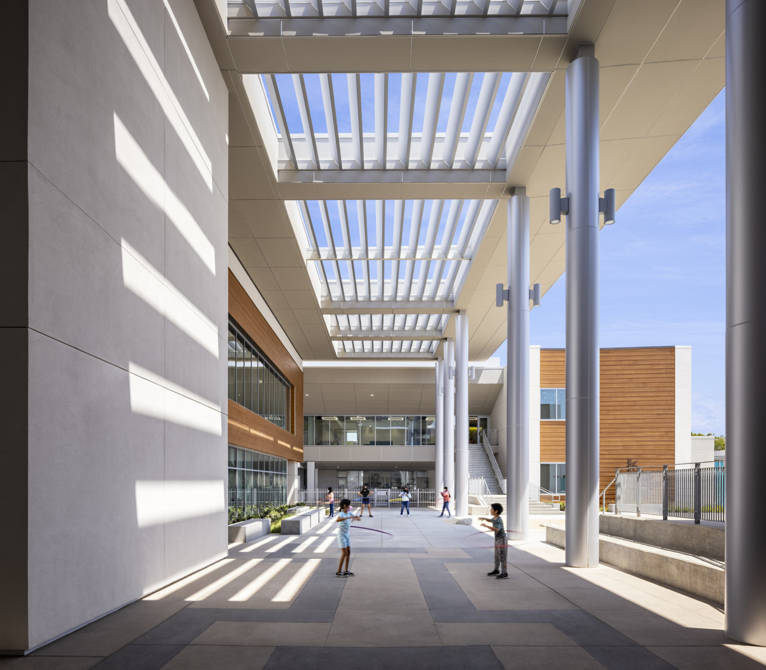 Front entrance of Logan Memorial Educational Campus partially covered under white canopy; a 2nd floor walkway right of a large staircase to upper level; modern and bright school design
