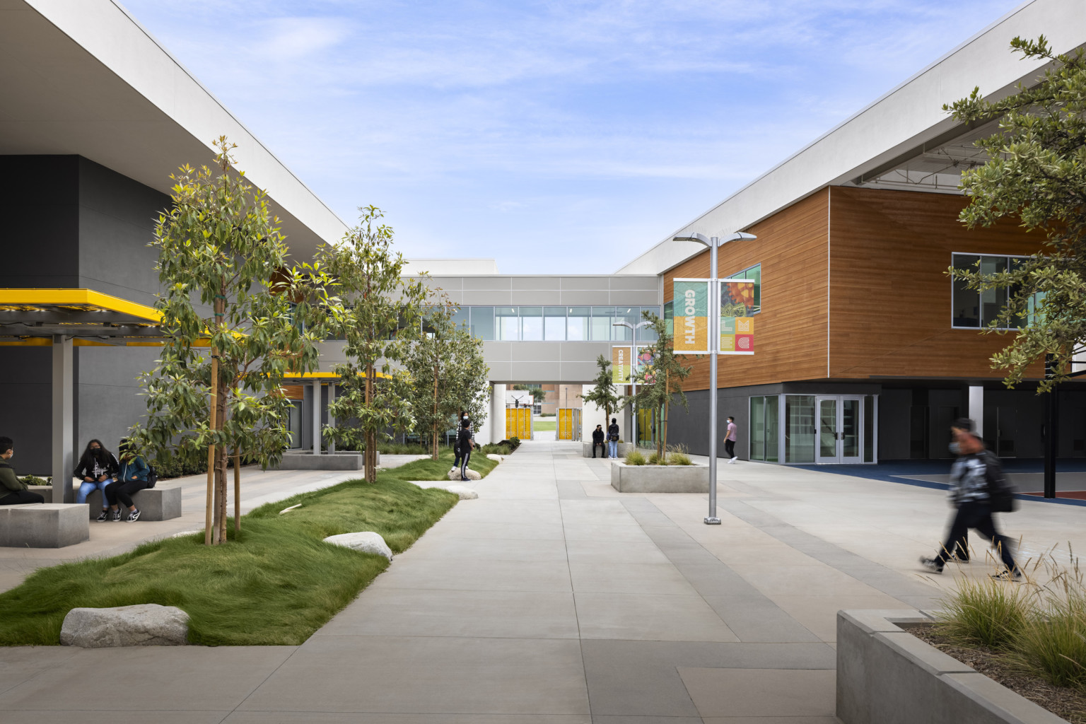 Exterior tree lined walkway on Logan Memorial Education Campus; Grey walls with white at the top, and a wood panel accent on right upper wall