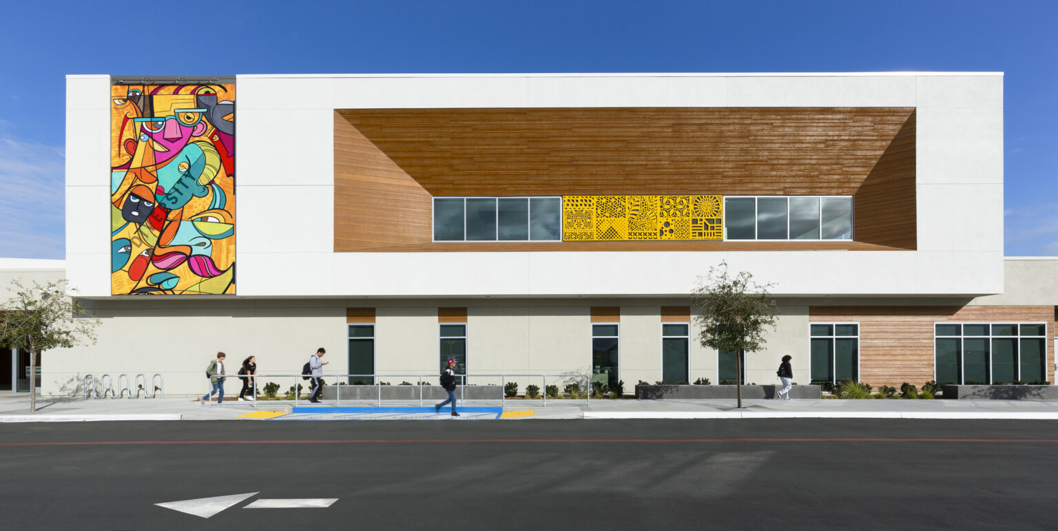 exterior shot of Logan Memorial Educational Campus; school design with bright mural; mass timber and white building façade; students walking in front of the building