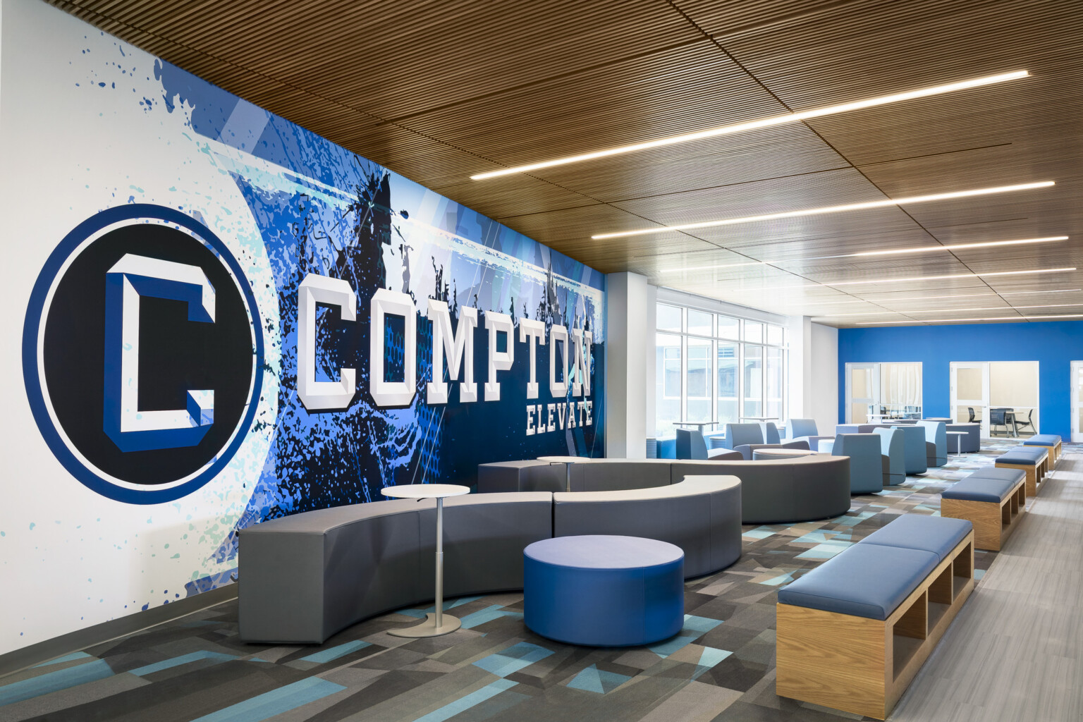 Common area of Compton High School; blue and white graphic design feature wall with "Compton" highlighted; community based-design seating