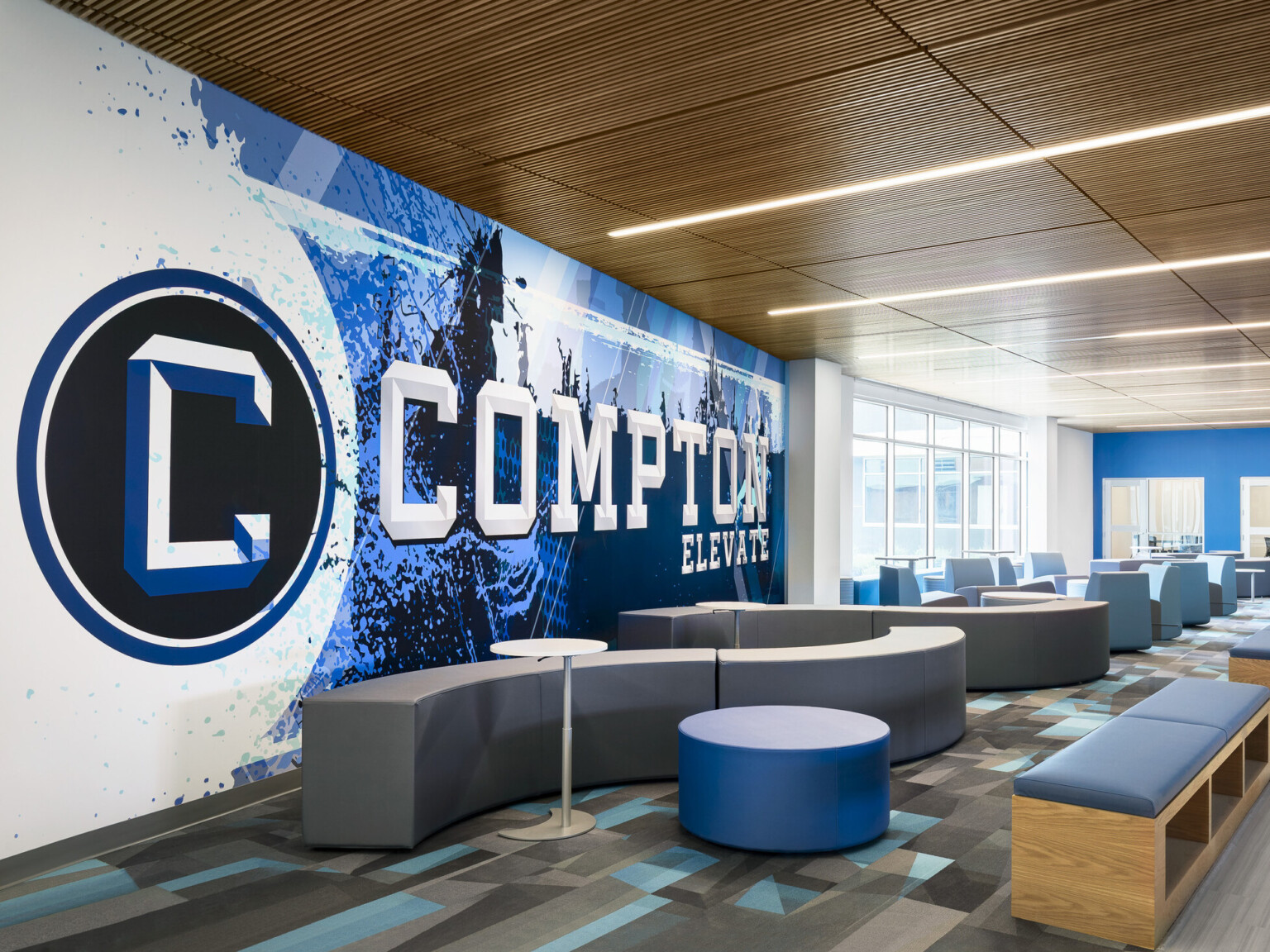 Common area of Compton High School; blue and white graphic design feature wall with "Compton" highlighted; community based-design seating