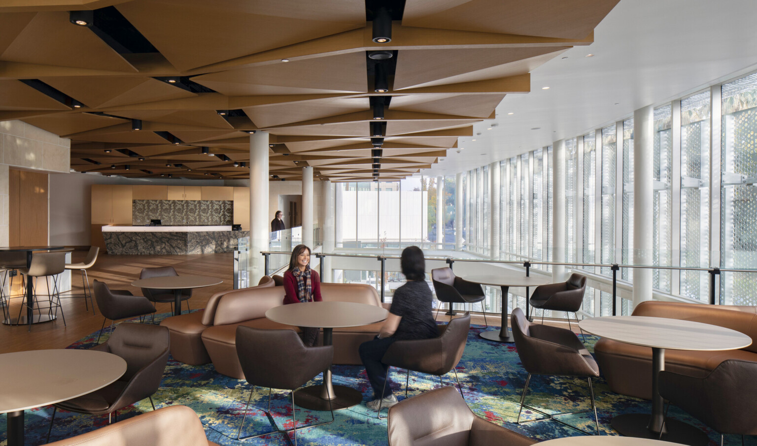 Multicolored carpet in a seating area with brown tables and chairs on inside balcony with brown structural geometric overhang