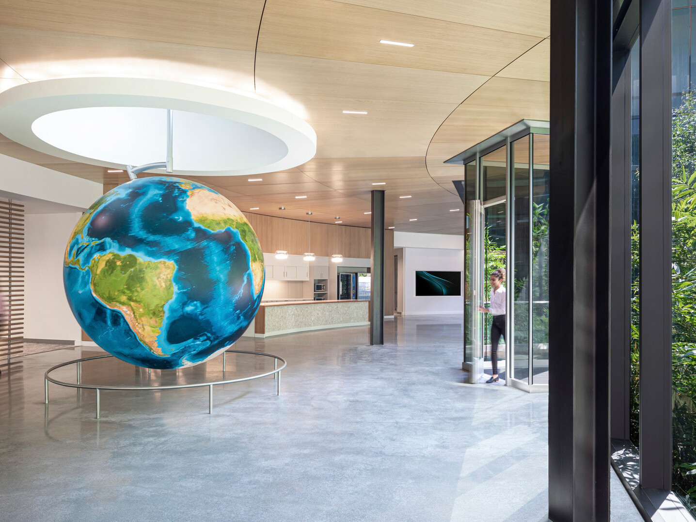 Curved hallway with floor to ceiling windows and wood panel ceiling. Round white recessed ceiling detail with hanging globe