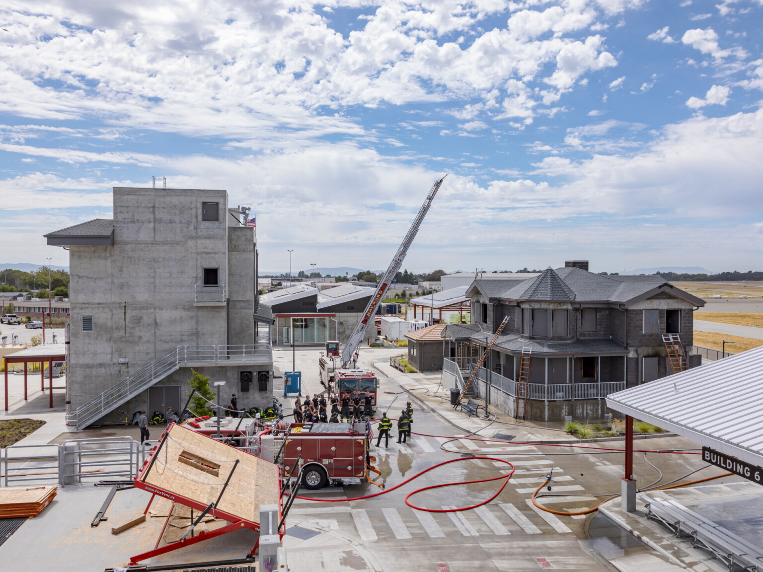 Fire training facility with multiple training areas of a large concrete building, Victorian house and other buildings in the background.