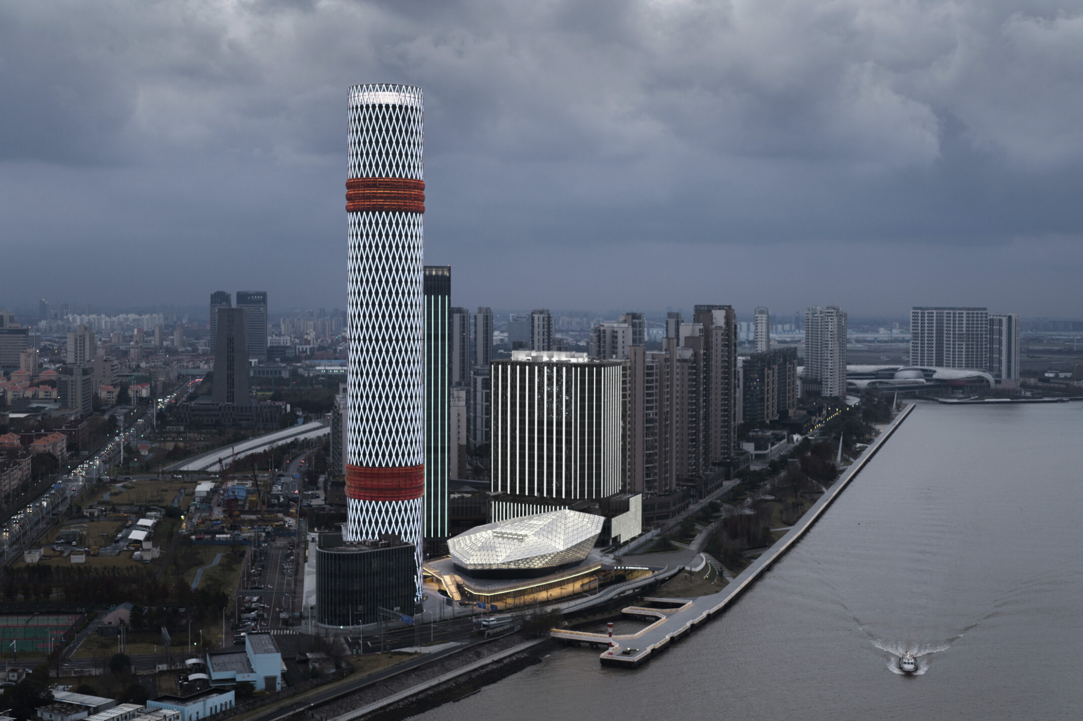 Baoshan Long Beach Complex illuminated at night along Shanghai's Yangtze River, diamond geometric light on cylindrical tower