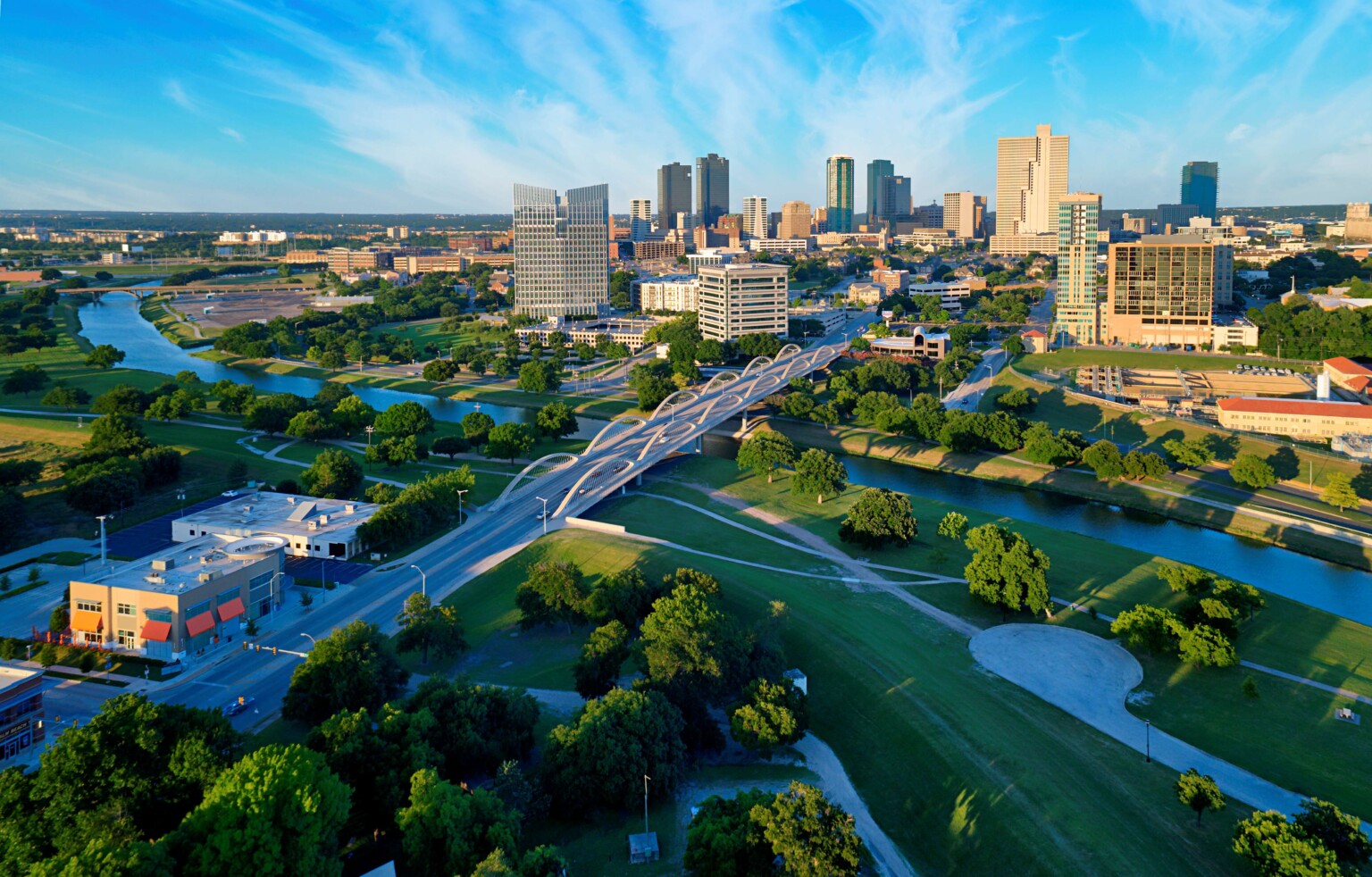 aerial view of the skyline of Fort Worth, Texas; a river winds around the city with skyscrapers and greenery in view