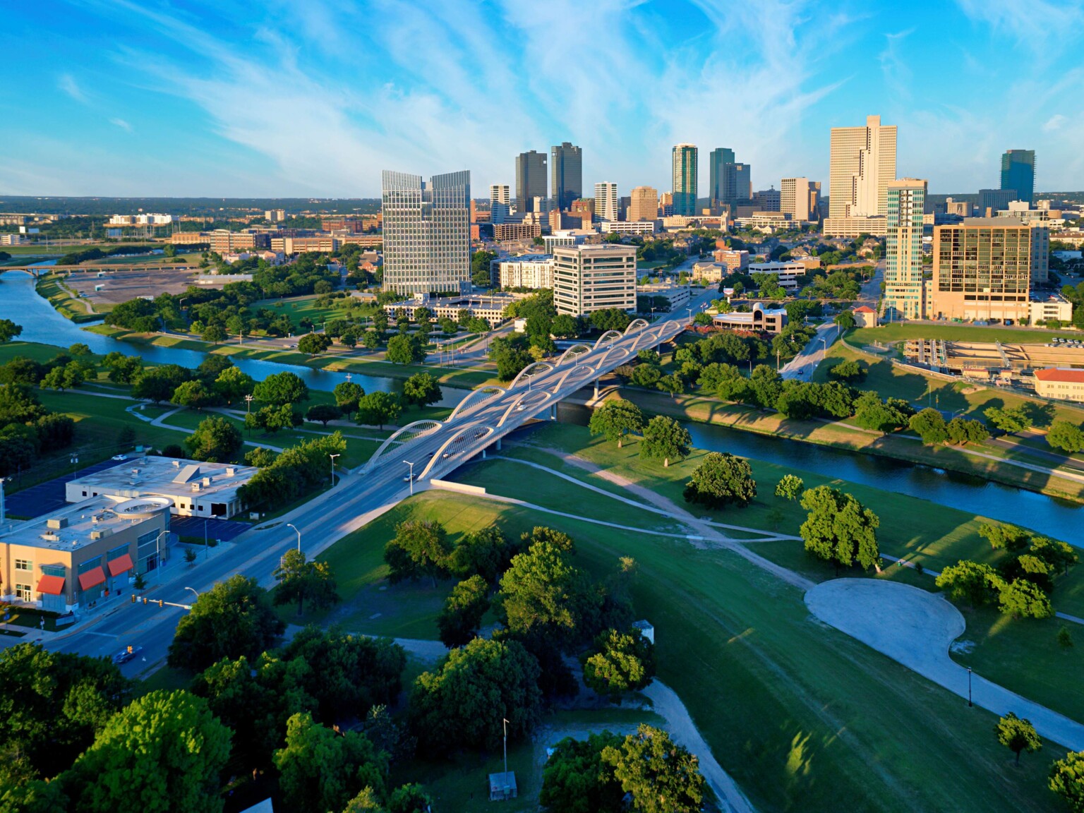 aerial view of the skyline of Fort Worth, Texas; a river winds around the city with skyscrapers and greenery in view