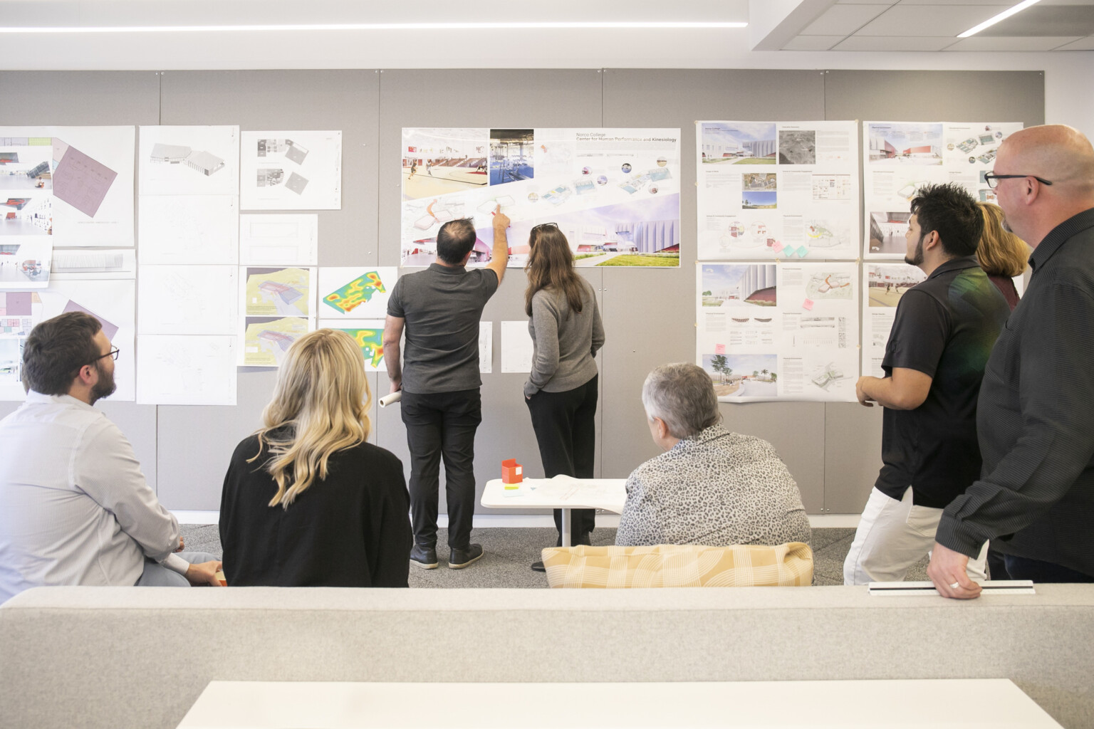 design leaders going through drawings together; sketches and architectural plans pinned up on wall
