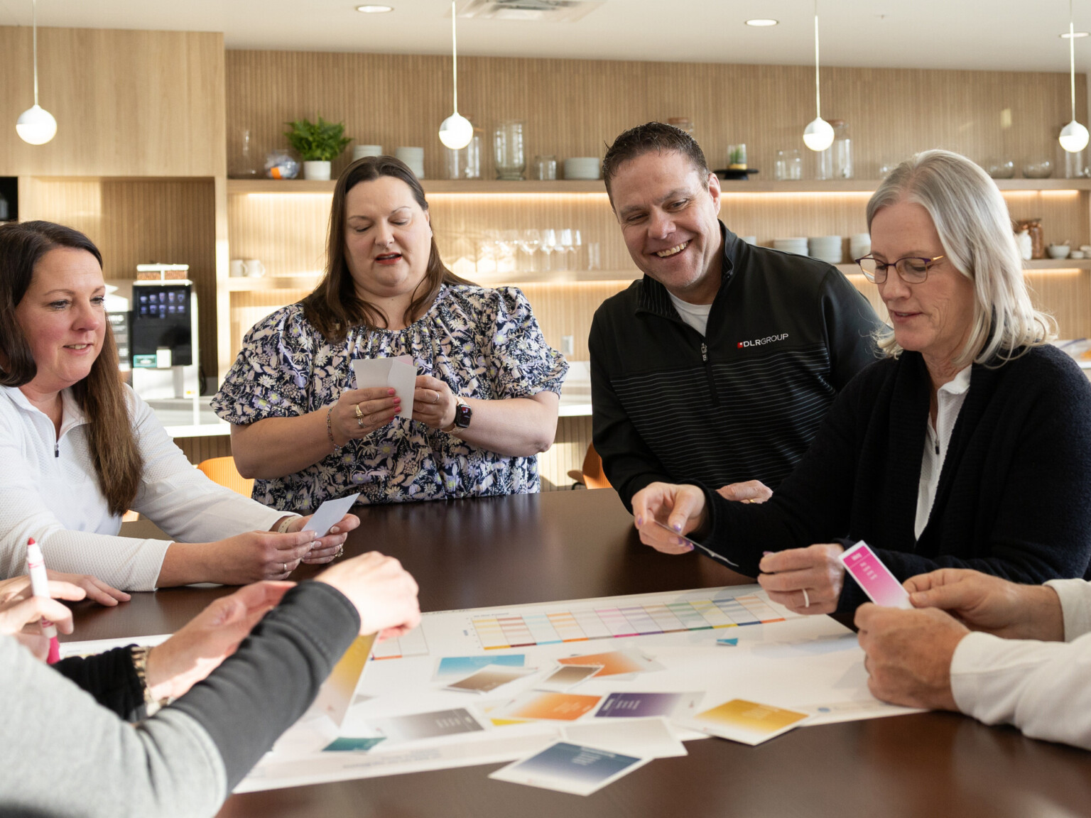 a group of adults huddled around a corporate office kitchen collaborating with paper cards and a full page spread